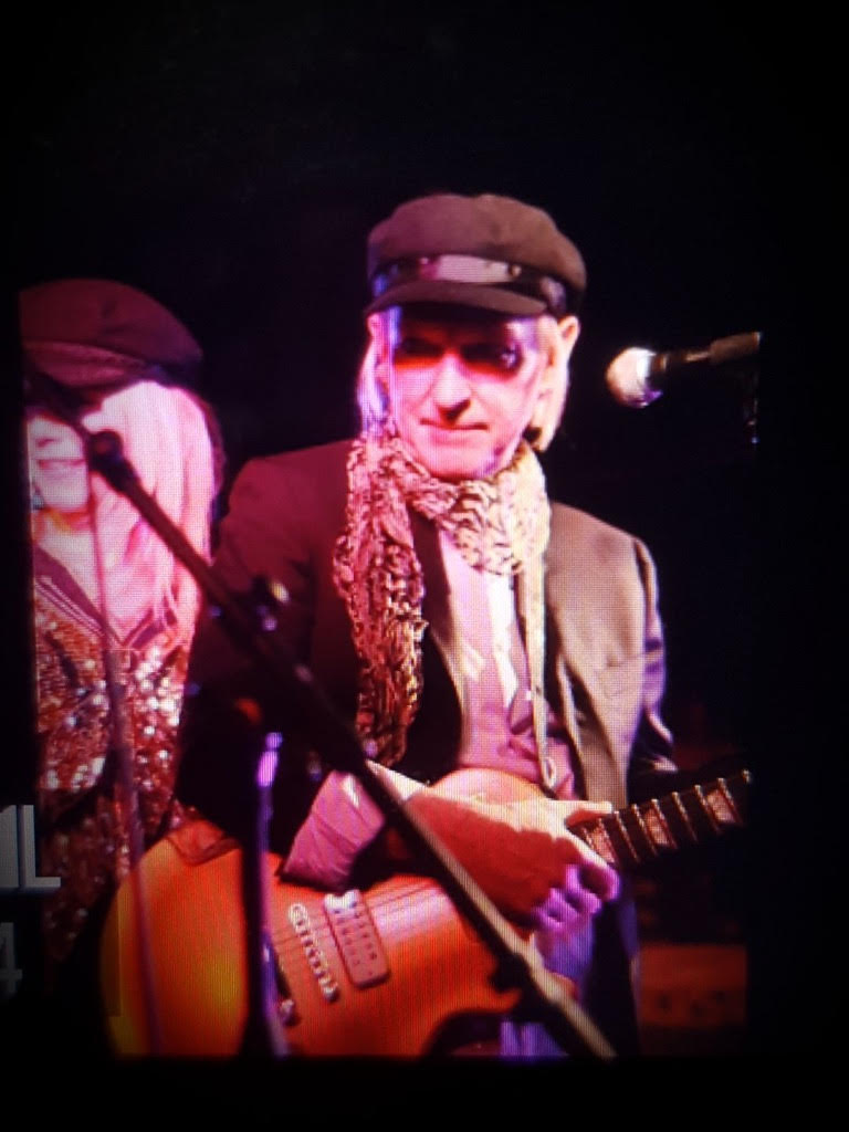 Billy Bloody Blake on stage with his guitar under pink stage lights